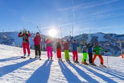 Kindergruppe steht nebeneinander und halten freudig ihre Skistöcke in die Luft